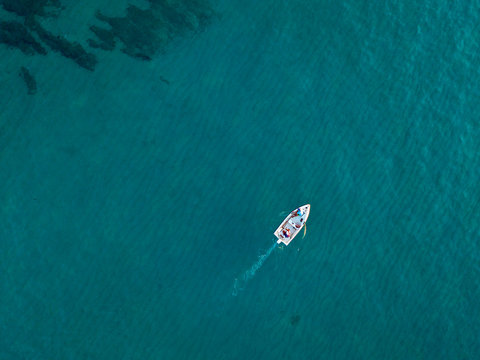 Aerial view of a rowing boat seen from above, powered by an engine. Blue sea that surrounds a boat that crosses it. People inside a boat. 10/22/2019. Pizzo Calabro, Calabria, Italy - Powered by Adobe