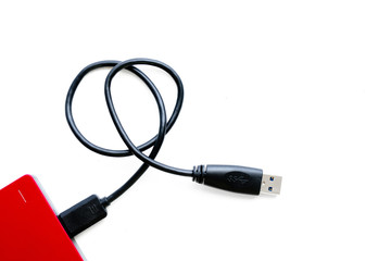 Modern red external hard disc with black cable for connected to computer isolate on white background.