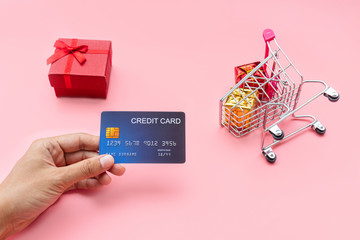Hand holing credit card, shopping cart with gift boxes on pink background. Shopping, shopping...
