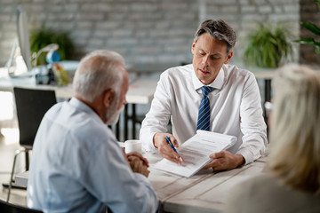 Insurance agent and senior couple analyzing terms of a contract while meeting in the office.