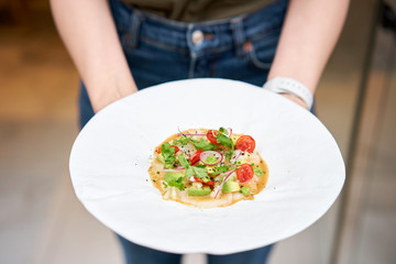 The waiter holds in his hands Tartar from scallop with avocado, cherry tomatoes, radishes and onion. Dish in the restaurant from raw seafood.