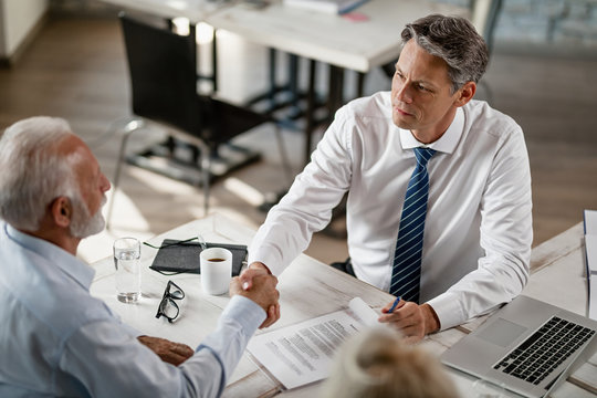 Above view of insurance agent and senior man shaking hands in the office.