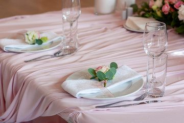 A pink tablecloth lies on the set table. The white napkin on the plate is decorated with a flower