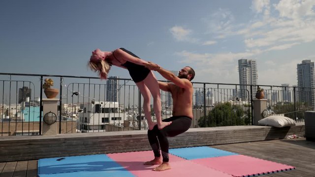Man and woman practicing acro yoga together, on a rooftop. Modern urban skyline in the background.