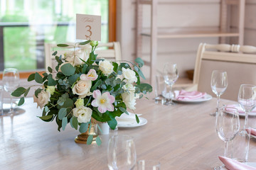 Number three. A white bouquet of flowers in a gold vase stands on a wooden table in the restaurant.