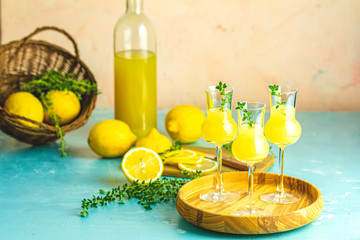 Limoncello with thyme in three grappas wineglass in wooden tray, fresh lemon in basket on light...
