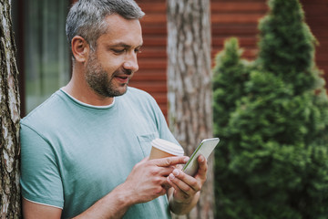 Handsome man with hot drink using cellphone outdoors