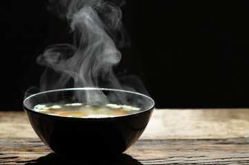 Hot soup with steaming and smoke in black bowl on wooden table with dark background. hot food concept.