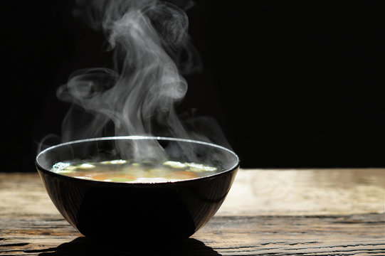 Hot Soup With Steaming And Smoke In Black Bowl On Wooden Table With Dark Background. Hot Food Concept.