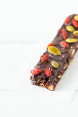 Vegan chocolate bars with granola,  goji berries, nuts, pumpkin and chia seeds. Homemade snack. Super energy bars on a white wooden background.