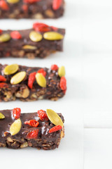 Vegan chocolate bars with granola, nuts, pumpkin and chia seeds. Homemade snack. Super energy bars on a white wooden background.