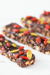 Vegan chocolate bars with granola, goji berries, nuts, pumpkin and chia seeds. Homemade snack. Super energy bars on a white wooden background.