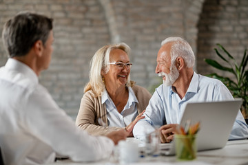 Happy senior couple talking to each other while having meeting with financial advisor.