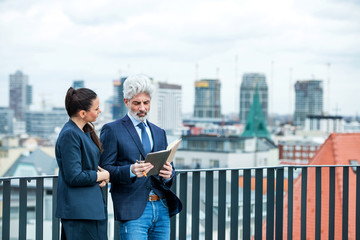 A businessman and businesswoman with diary standing on a terrace, working.