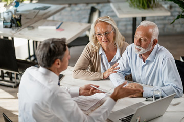 Senior couple talking to real estate agent on a meeting in the office.