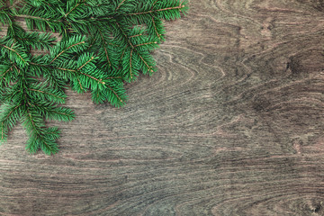 Natural Christmas background with border of fluffy green fir branches on a textured dark brown wood background. Copy space for text, flat lay, top view. Corner frame.