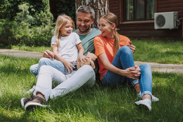 Beautiful happy family sitting on green grass outside the house