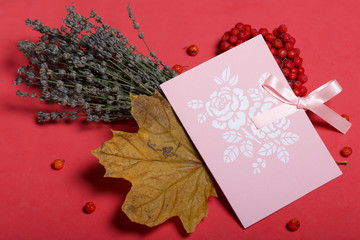 Greeting card and a bunch of mountain ash with a dry maple leaf. Near a bouquet of lavender. Autumn still life. Against the background of coral color.