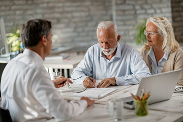 Mature couple signing a contract on a meeting with bank manager.