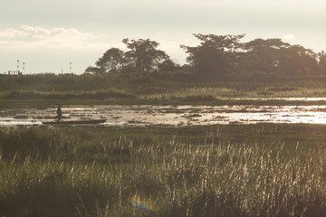 silhouette of a man in a boat, which is on the river in the middle of the field, a filter is applied to the photo