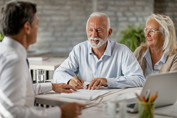 Happy senior couple signing an agreement while having a meeting with financial advisor. - obrazy, fototapety, plakaty