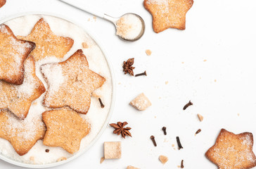Christmas homemade gingerbread cookie sprinkled with sugar in a plate and spices on a white background, top view. Traditional Christmas sweet pastries.