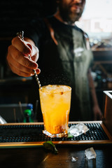 Bartender stirring a sweet and fresh orange summer cocktail in glass