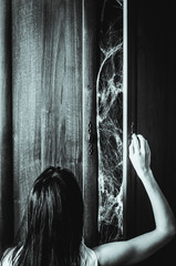 Fototapeta na wymiar Young woman opens a door of an old wardrobe with spiderweb something creepy inside