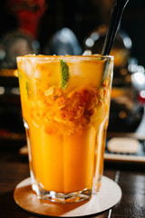 A orange drink in a glass with ice cubes, orange,straw and mint leaves