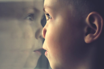 Little boy looking through window. Reflection of the face in the glass.