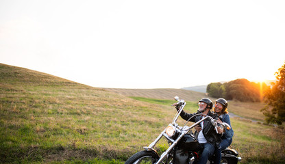 A cheerful senior couple travellers with motorbike in countryside. © Halfpoint