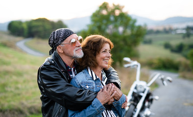 A cheerful senior couple travellers with motorbike in countryside.