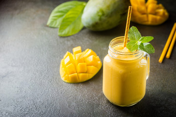 Refreshing and healthy mango smoothie in a glass with fresh fruit over stone background with copy space