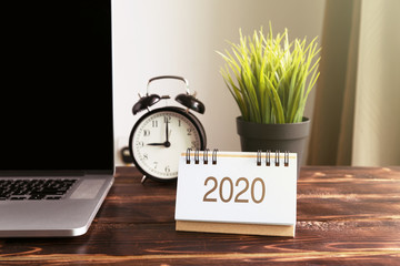 New Year 2020 calendar on office desk with laptop and alarm clock