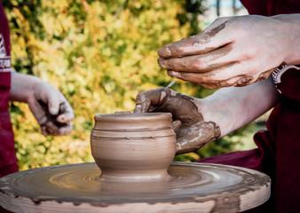 Master class of clay making, pottery workshop outside, hands of potter creating a jar on potters wheel, one person teach another co-creation