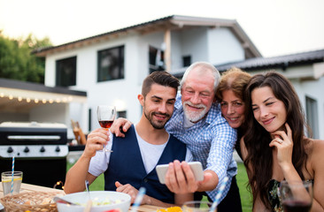 Portrait of people outdoors on family garden barbecue, taking selfie.