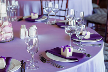Table setting. Lilac tablecloth on the table. White plates with party favors.