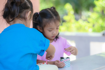 The kindergarten of two sharp Asian girls eating cake