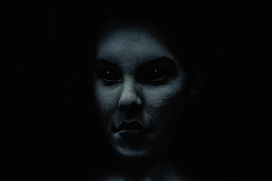 Scary and frightening  demonic woman face with black eyes in the dark.  Diabolic  and possessed by evil spirit young girl. Halloween look.