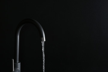 Closeup view of water flowing from faucet on black background. Space for text