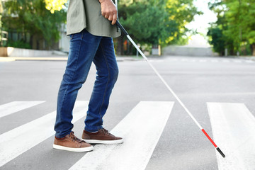 Blind person with white cane crossing street in city, closeup