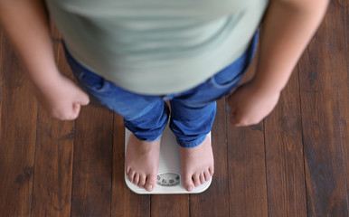 Overweight boy standing on floor scales indoors, above view © New Africa