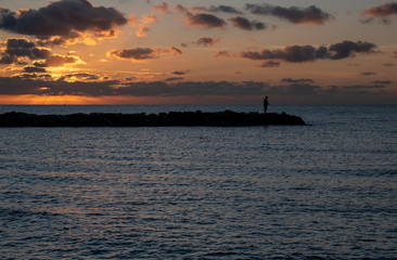 Beautiful Sunrise in Mallorca with a person fishing on the sea defences.
