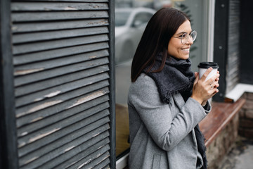 Portrait of a young woman in glasses. A young business woman stands at the window of a cafe and drinks coffee