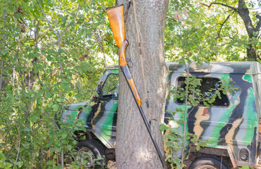 Hunting rifle hanging on a tree near an SUV