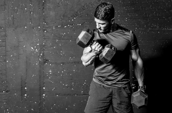 Young strong muscular sweaty man biceps muscle workout training with heavy dumbbell weight in the gym dark image with shadows real people black and white