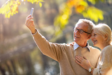 Naklejka premium Senior couple taking selfie with smartphone in park