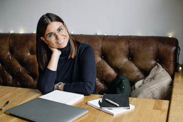 Young business woman sitting at table and taking notes in notebook.On table is laptop, smartphone...