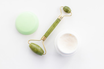 Massage roller for the face with two heads of jade stone and jar of face cream.