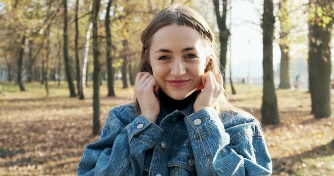 Portrait of young attractive female who smiling and looking at the camera on autumn park. Cheerfully pretty woman at sunny weather. Close up